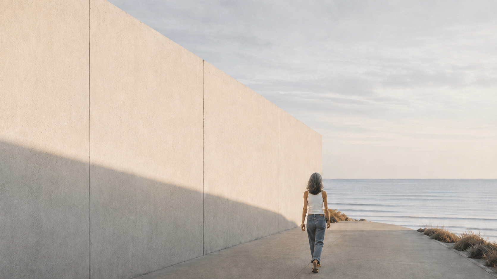 A woman walking quietly beside a long concrete wall by the sea