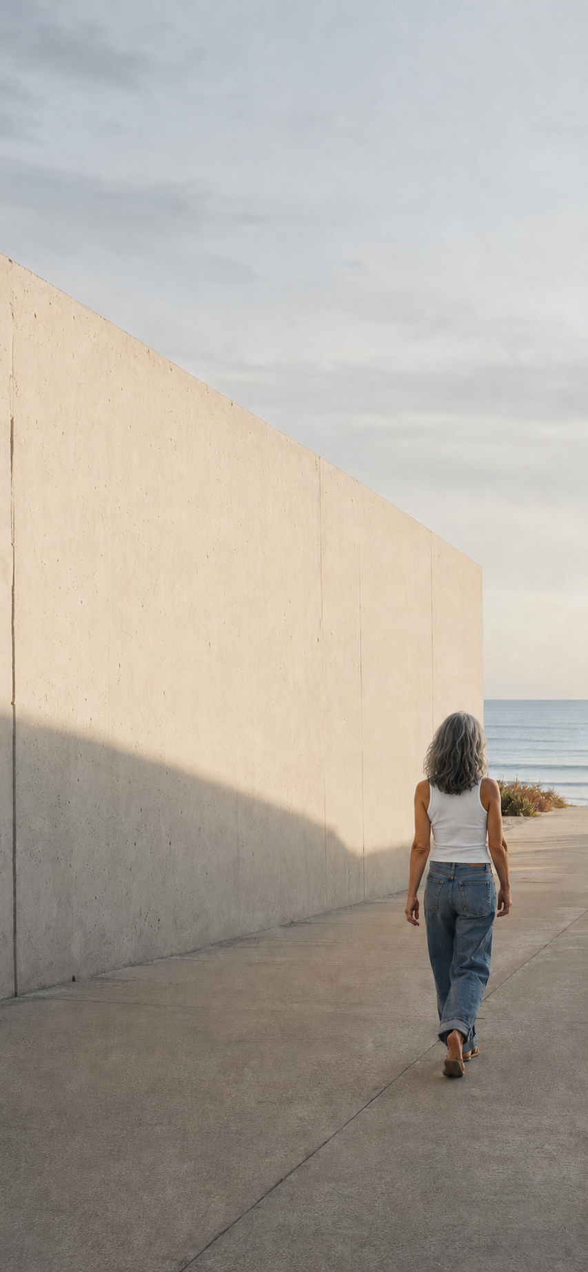 A woman walking quietly beside a long concrete wall by the sea