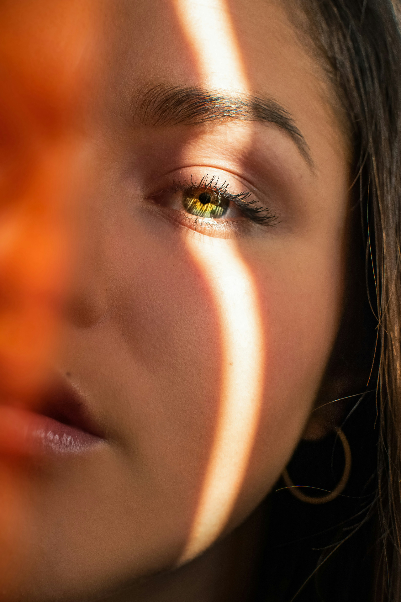 Close-up of a woman's face lit by a band of sunlight, looking quietly into the distance.